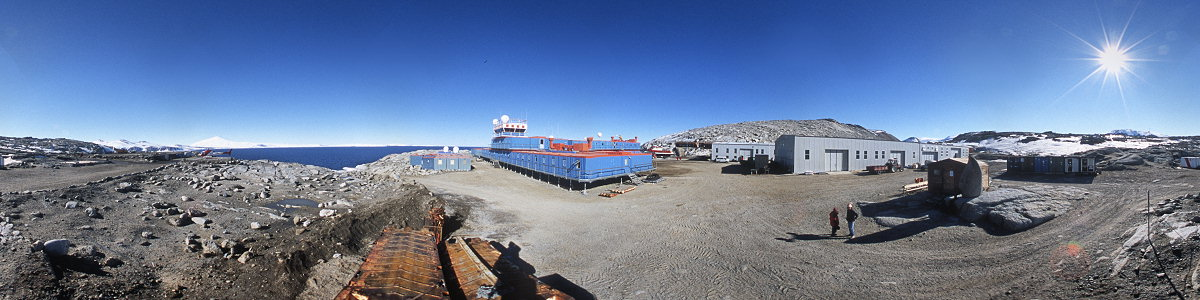 [BTNplaceBPano_.jpg]
Panoramic view of the station, taken from between the buildings, the shore and the helicopter pad. From Left to right: Helicopter and Mt Melbourne, main station building, garages and workshops, pinguinatolo and containers.