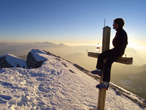 Skier taking in the view sitting on the summit cross of Chamechaude