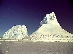 Two people at the base of a tall iceberg