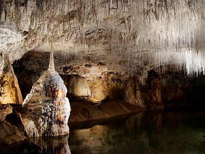 Fat stalagmite and thin stalactites above underground lake
