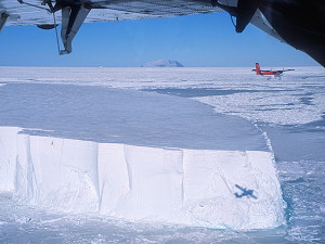 Twin Otters flying above large tabular iceberg